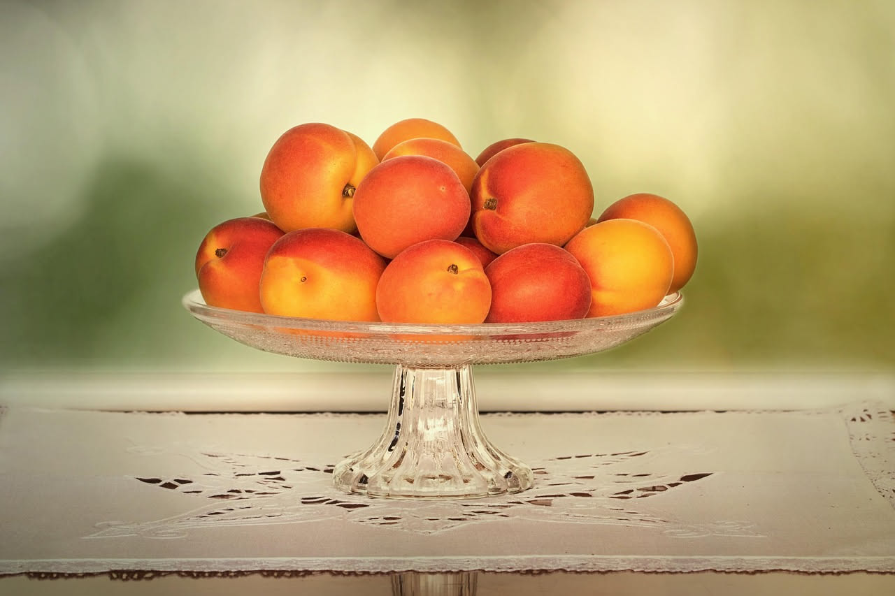 Albicocche mature color arancio intenso raccolte in una cesta di vimini su un tavolo di legno, con foglie verdi sullo sfondo e luce naturale estiva