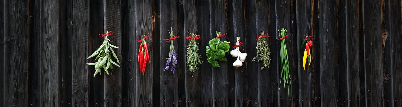 Fascetto di basilico, rosmarino e salvia appena raccolti, con gocce di rugiada, su un tavolo di legno al tramonto estivo