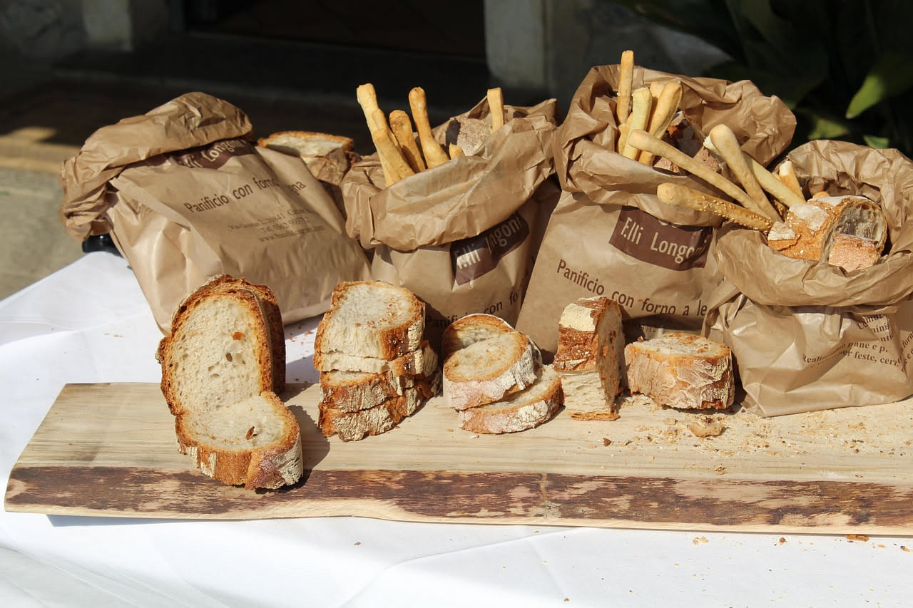 Pane toscano appena sfornato ancora tiepido, tagliato in fette, con crosta dorata croccante, accanto a una carta di pane e un canovaccio di lino bianco in una cucina estiva