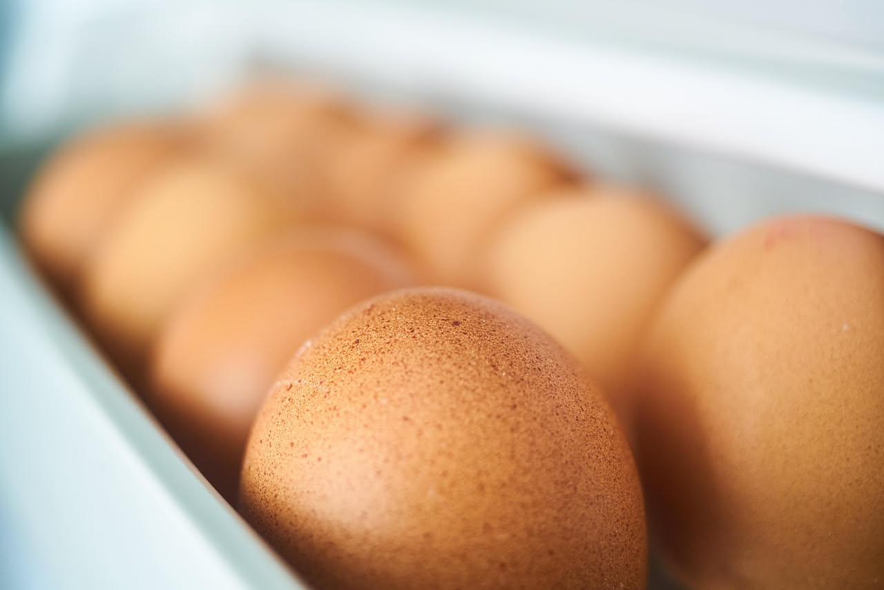 Uova bianche e marroni poste nel reparto delle uova del frigorifero, con termometro interno che segna 4 gradi, luce naturale del mattino