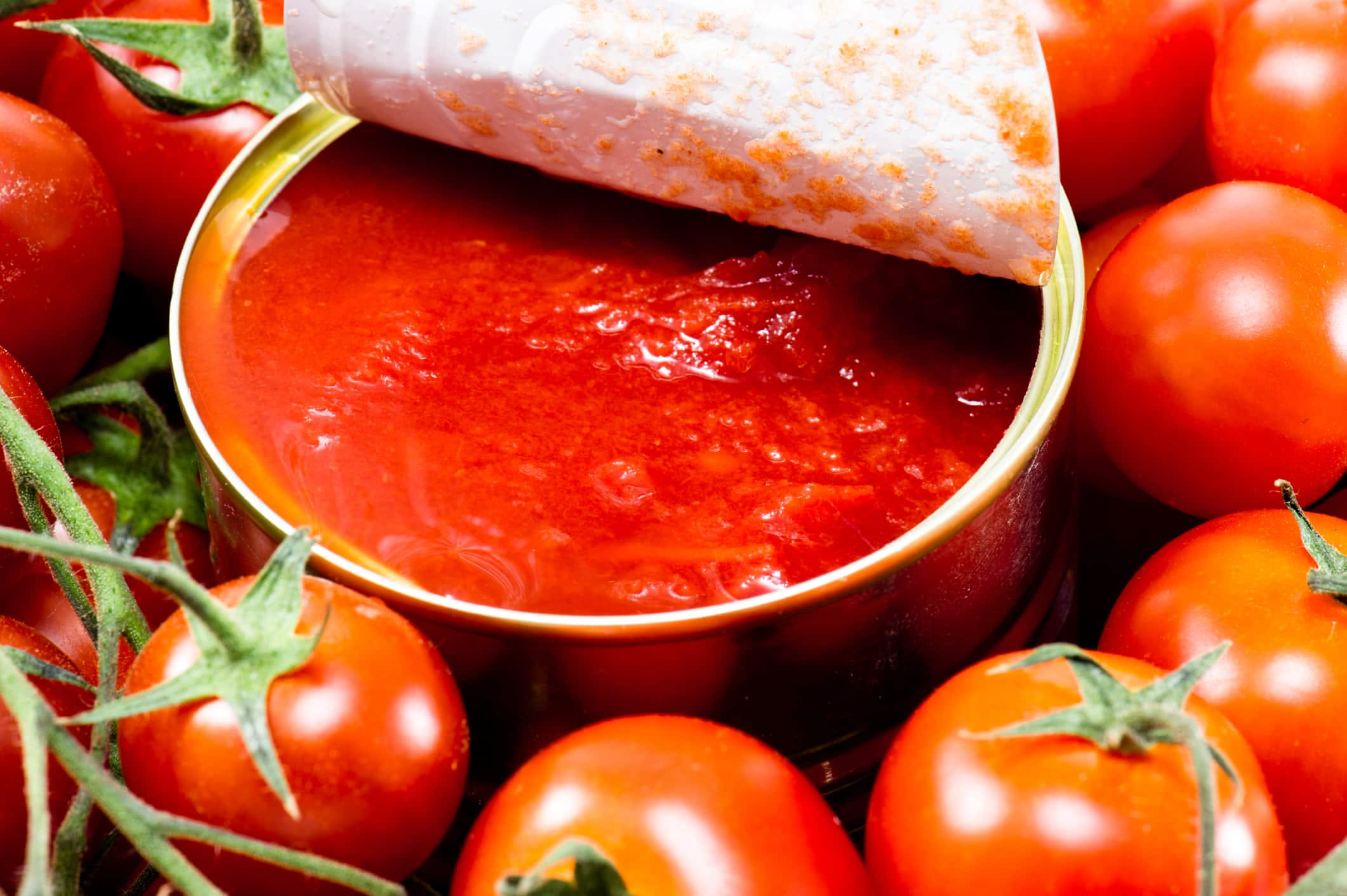 Bicchiere di vetro trasparente contenente acqua di pomodoro trasparente e leggermente rosata, con semi di pomodoro visibili sul fondo e una foglia di basilico accanto