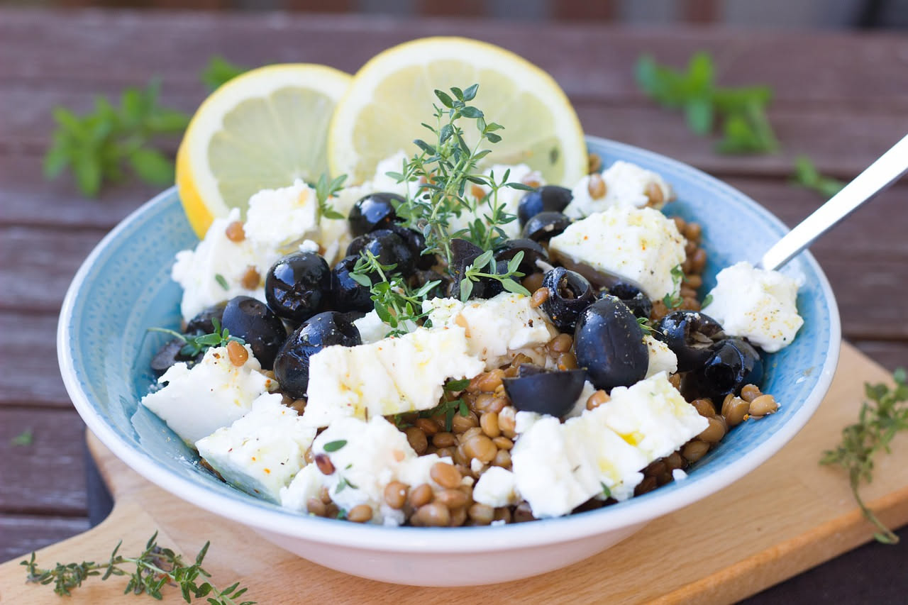 Insalata di farro fredda in ciotola di terracotta con verdure fresche, pomodori, cetrioli e erbe aromatiche su tavolo di legno bianco