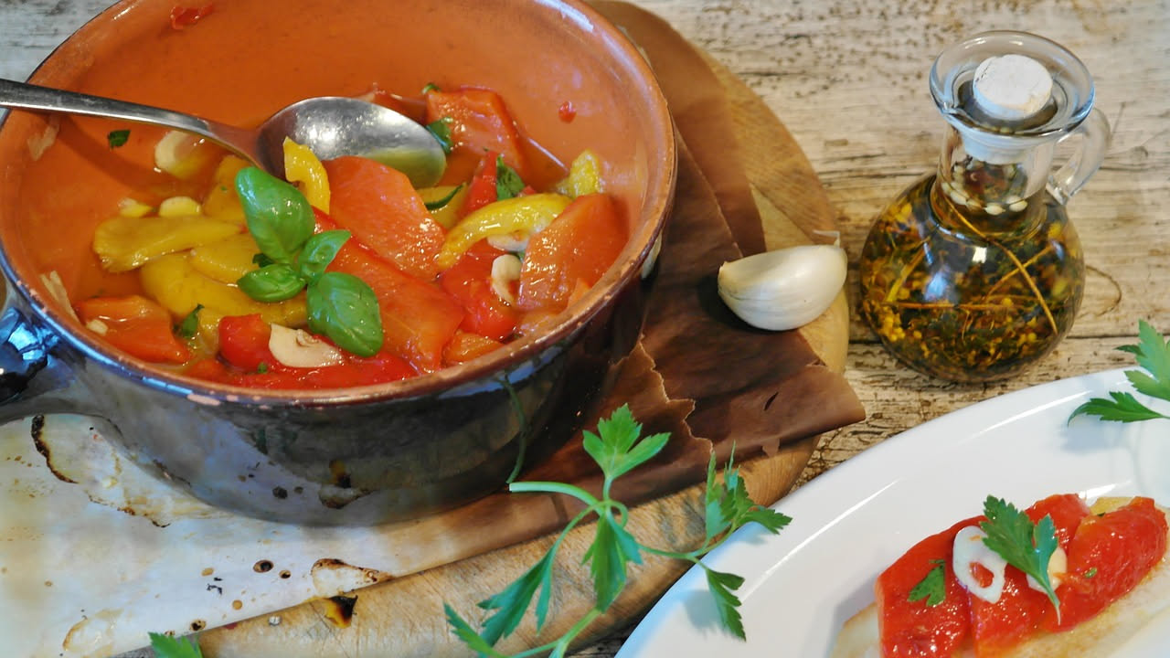 Caponata siciliana in piatto bianco con melanzane viola, pomodori rossi, olive nere, capperi e sedano su sfondo di cucina rustica