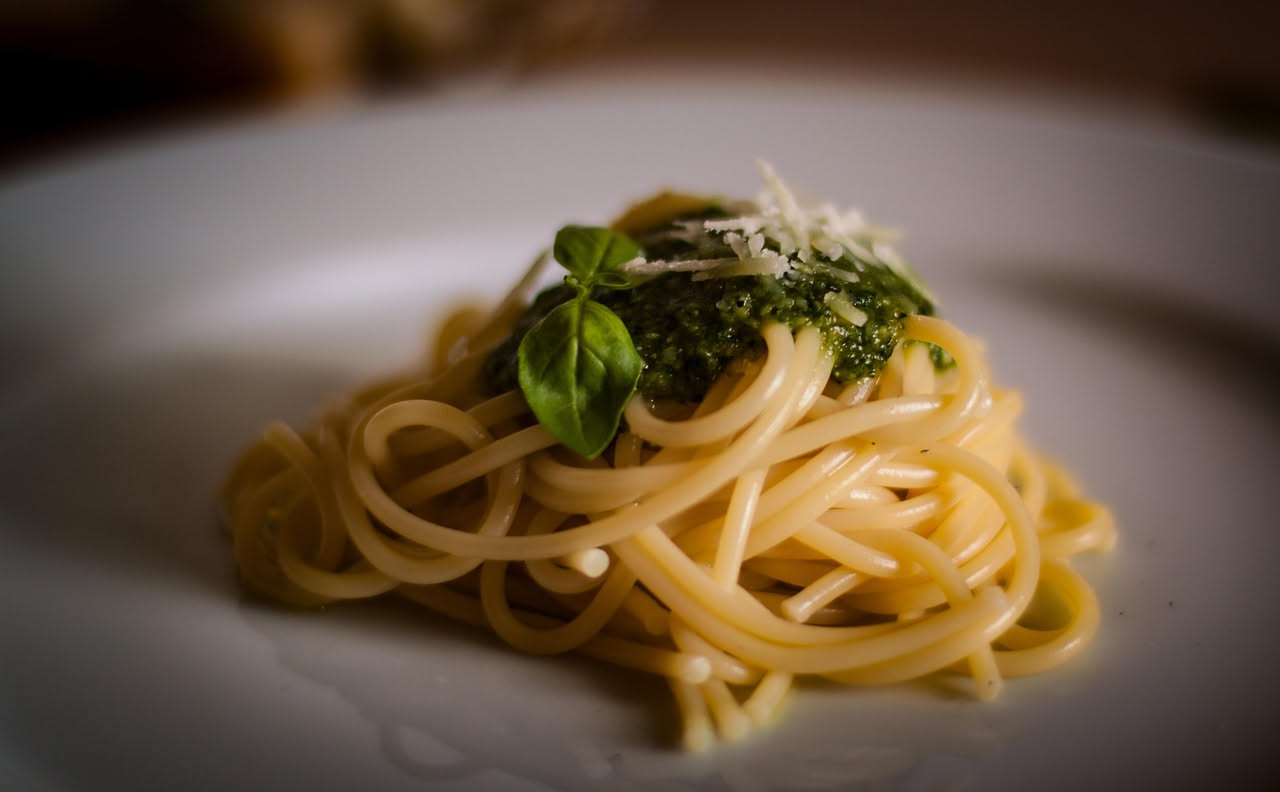 Mortaio in marmo con pesto verde brillante, basilico fresco, spicchi d'aglio bianco e pinoli su sfondo bianco, vista dall'alto