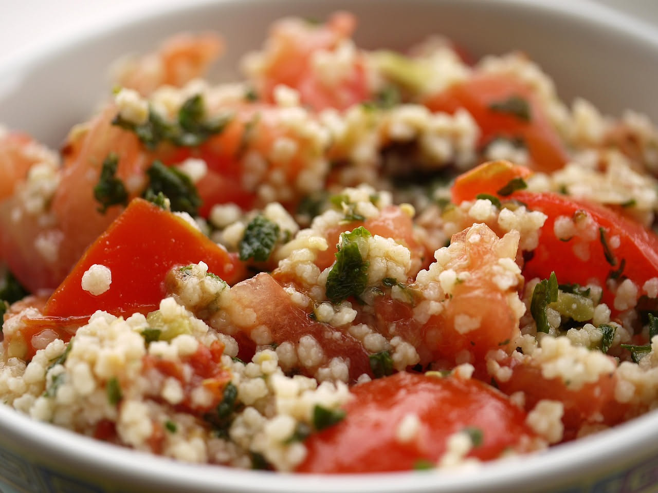 Ciotola di tabulè con bulgur, prezzemolo verde brillante, pomodori e limone, condito con olio d'oliva, su tavolo di legno naturale