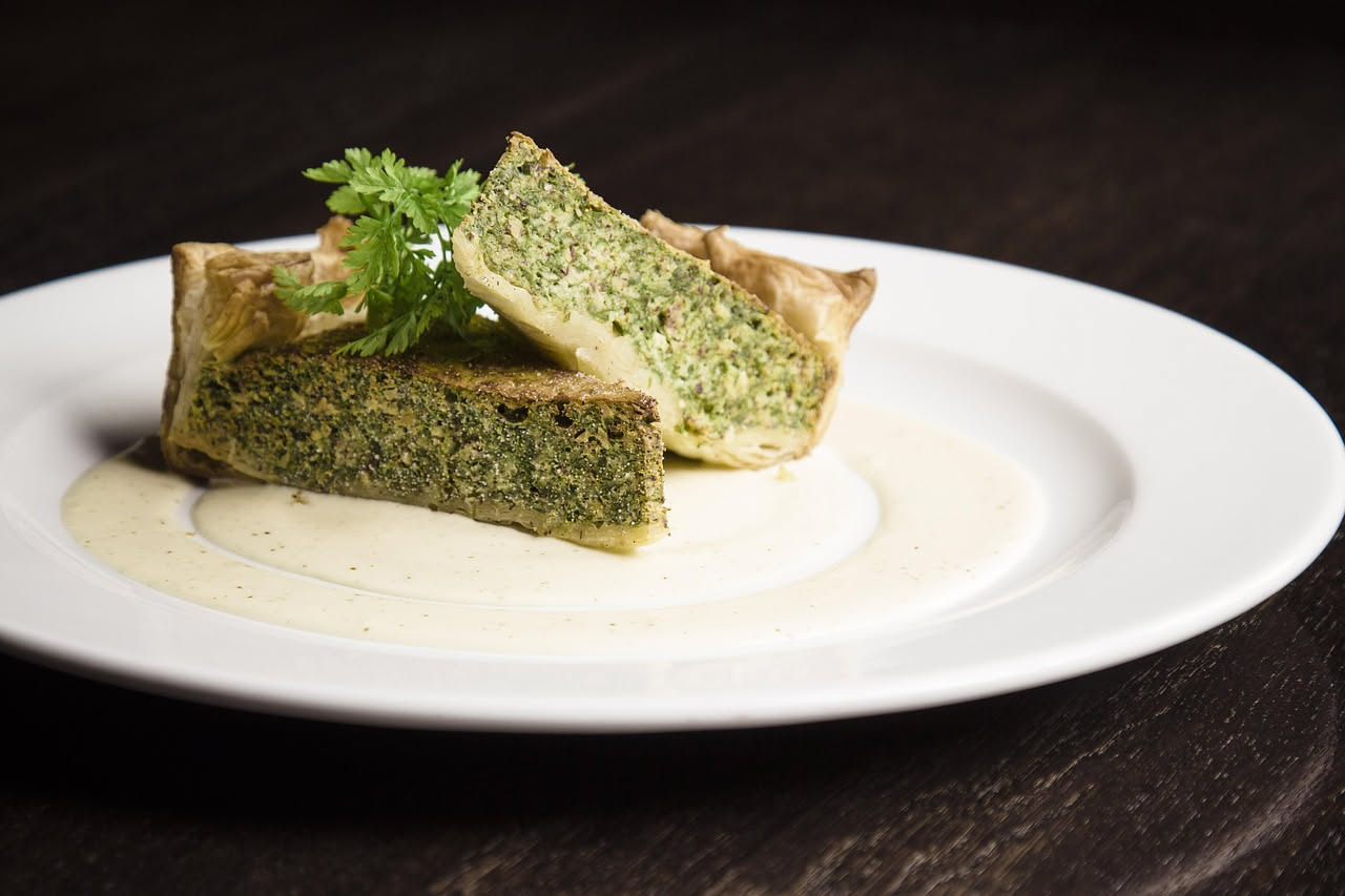Frittata rotonda dorata in padella, tagliata in spicchi, con zucchine verdi a fette visibili all'interno, guarnita con foglie di menta fresca verde sulla superficie, sfondo di legno chiaro