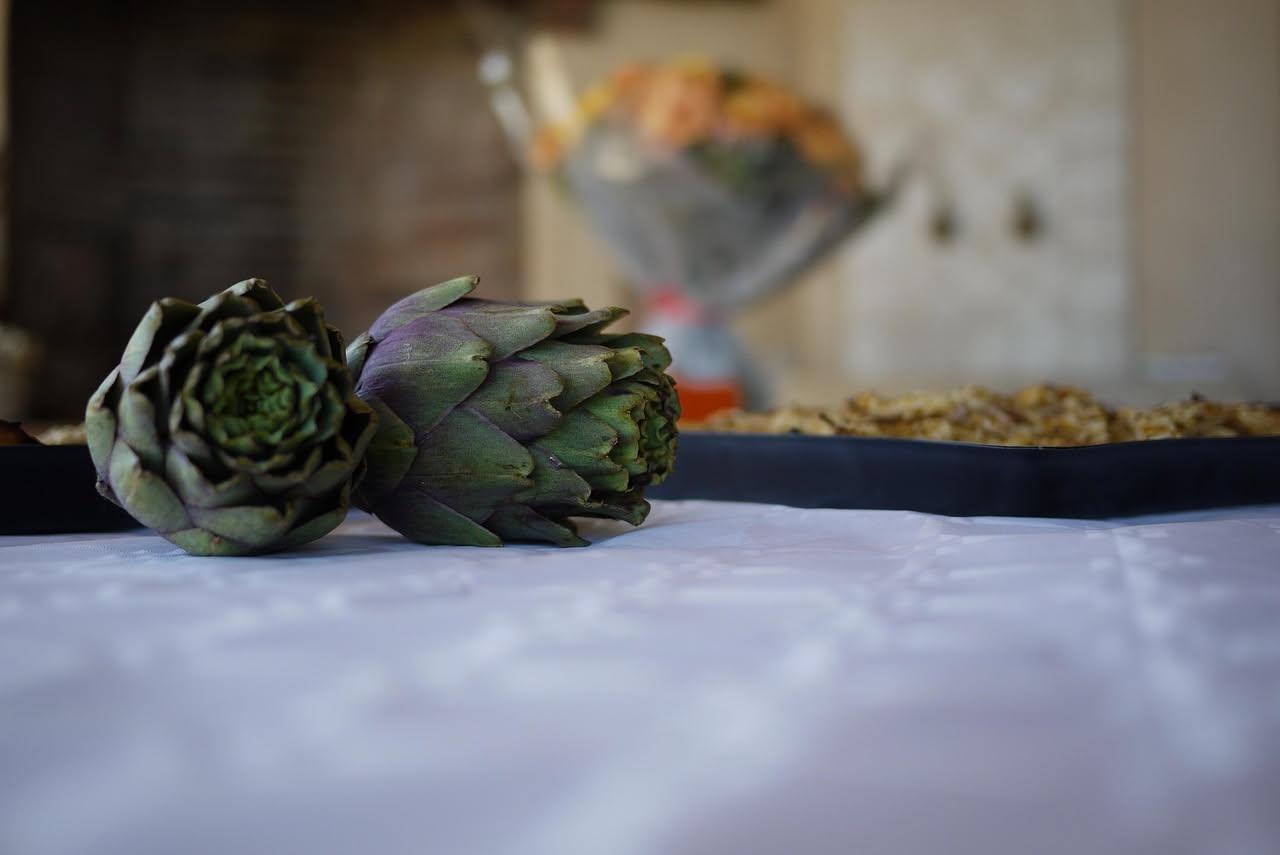 Carciofi freschi di colore verde scuro con spine evidenti, disposti su tavolo di legno rustico con foglie verdi in primo piano