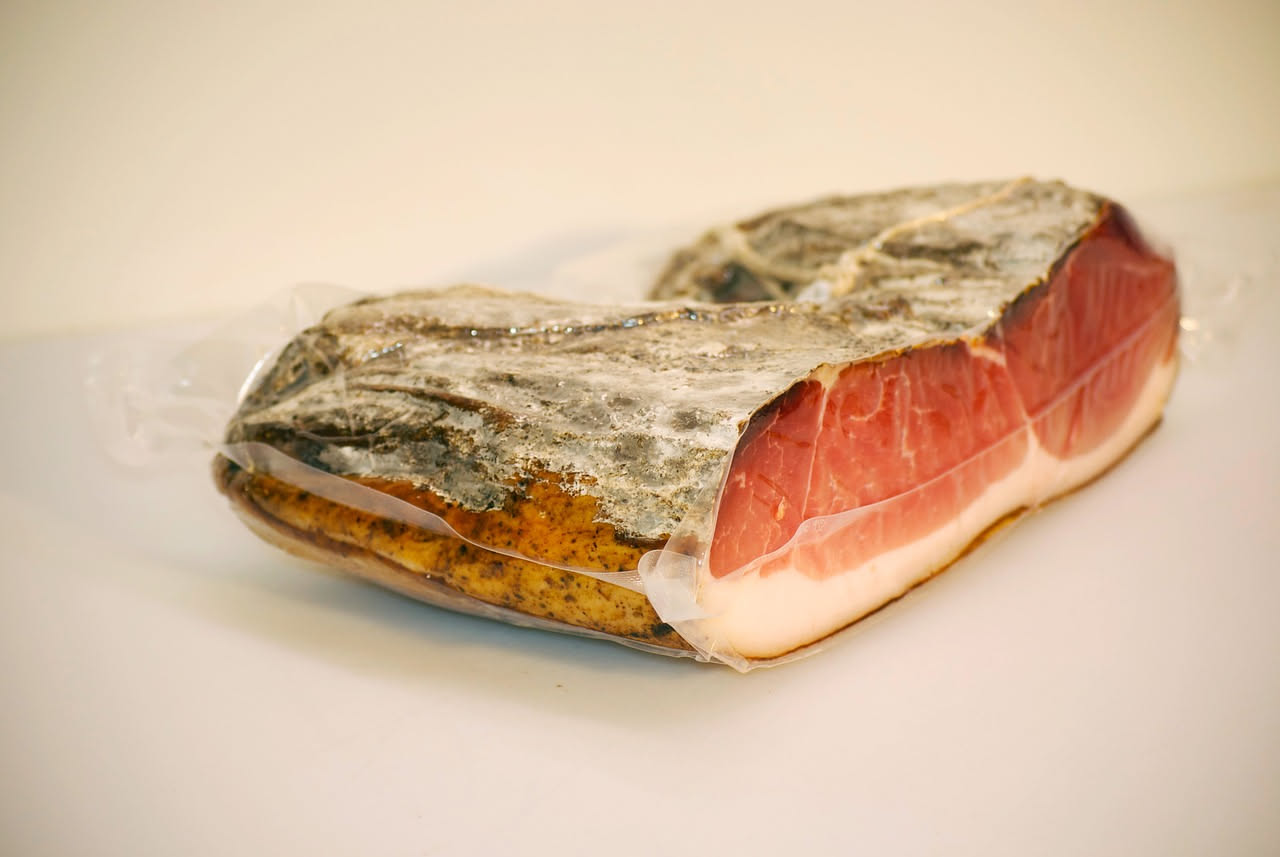 Fette sottili di guanciale rosso scuro con venature di grasso bianco, disposte a ventaglio su un piatto bianco