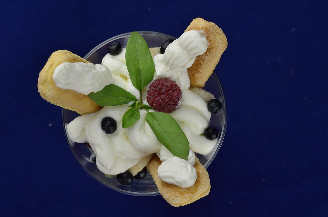 Mascarpone bianco cremoso in una ciotola di vetro, con un cucchiaio che ne preleva una porzione, accanto a fragole fresche e caffè in tazza