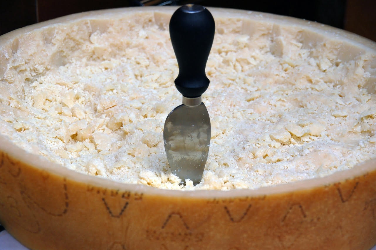 Pezzo di Parmigiano Reggiano maturo con la caratteristica frattura cristallina, tagliato a spicchio, con la tipica marchiatura a fuoco sulla crosta