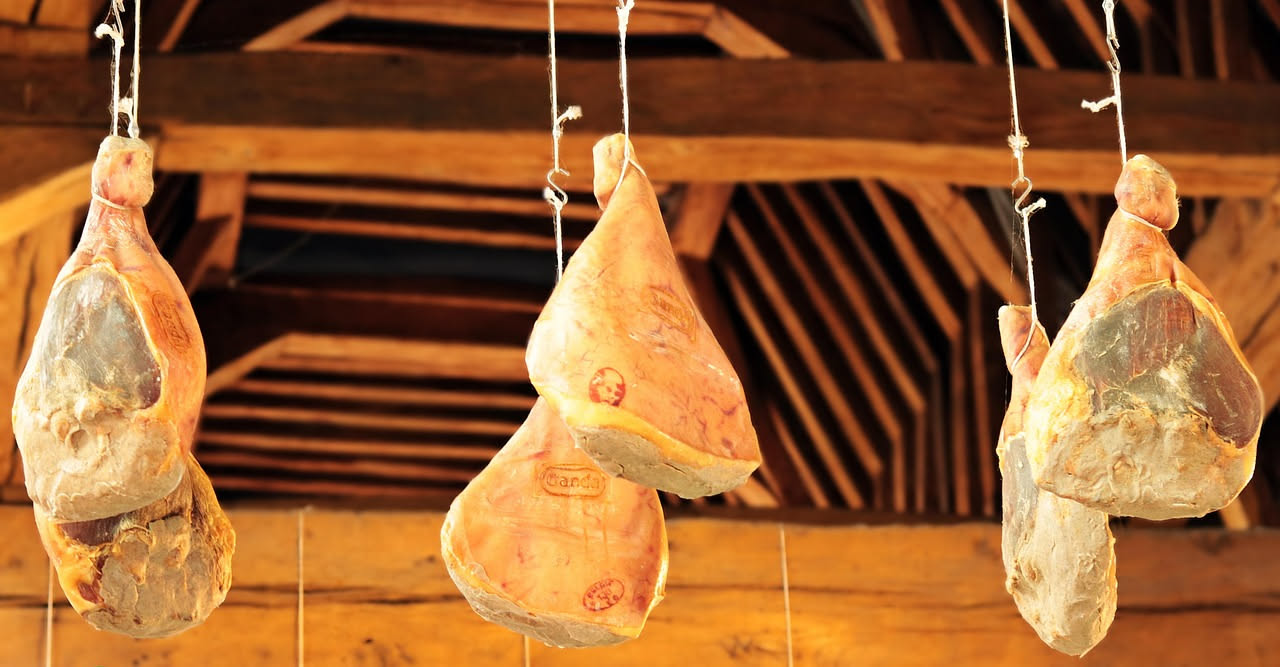 Fette di prosciutto di Parma color rosa dorato leggermente trasparenti, tagliate sottilmente, disposte su un piatto bianco con una bottiglia di vino rosso sullo sfondo