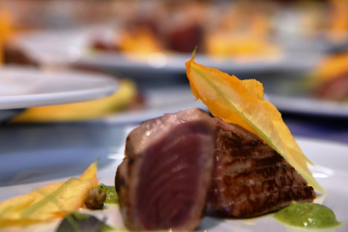 Filetto di tonno fresco rosso intenso con venature bianche, posato su superficie di marmo bianco con limone e erbe aromatiche