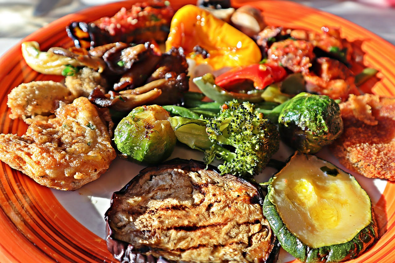 Insalata di farro con fette di zucchine, melanzane e peperoni grigliati color grigio scuro e marrone, presentata in una ciotola bianca con foglie di basilico fresco, condimento all'olio visibile e gra