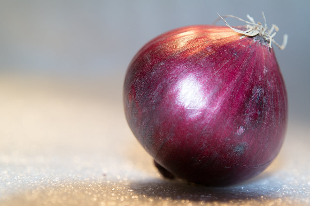 Cipolle gialle, rosse e bianche appena tagliate su una tavola di legno, con gli strati interni ben visibili e una ciotola di acciaio