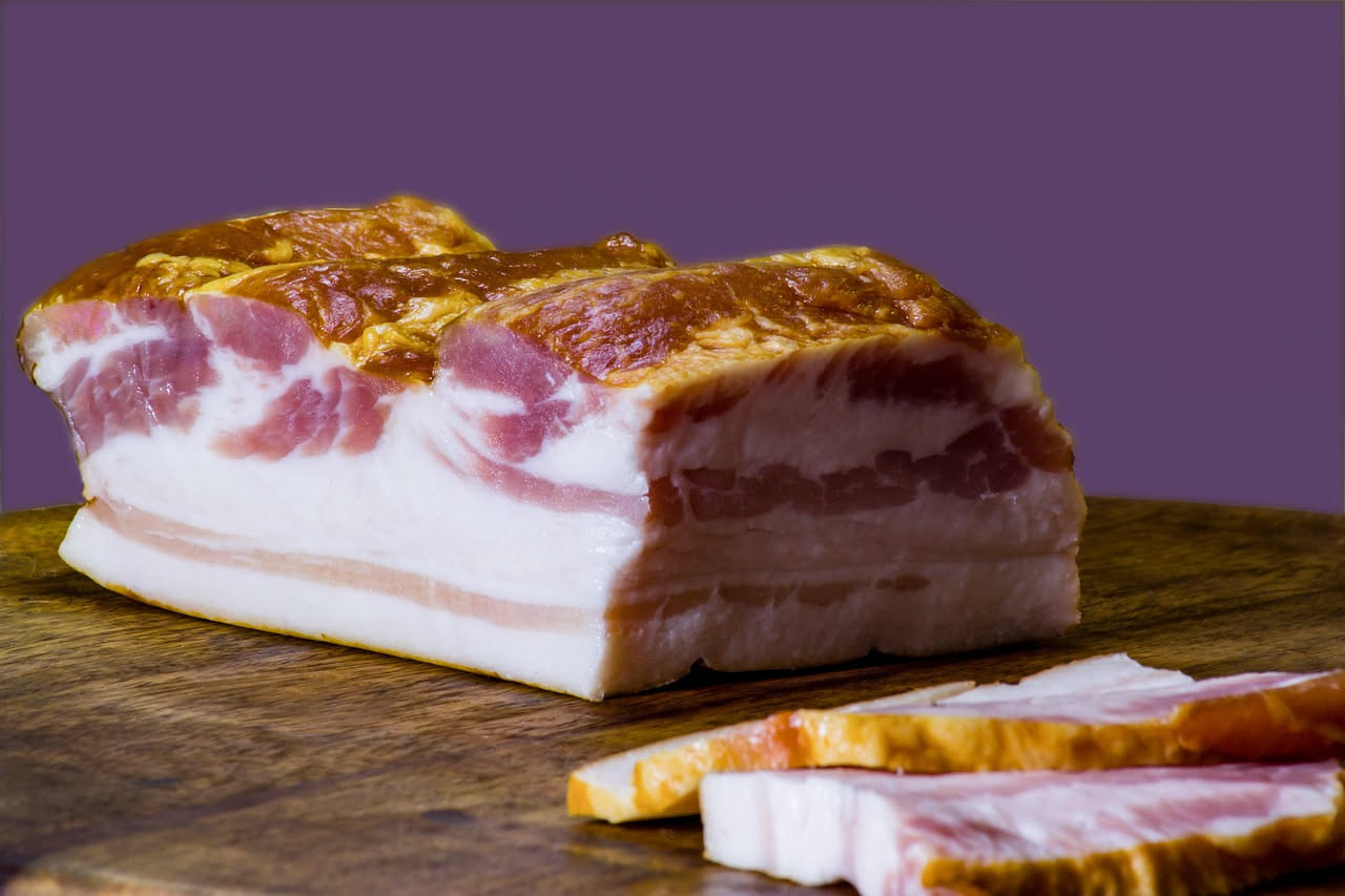 Affettato sottile di pancetta arrotolata, mostrando i strati di carne e grasso con colorazione rosata e sfumature bianche, su un tagliere di legno