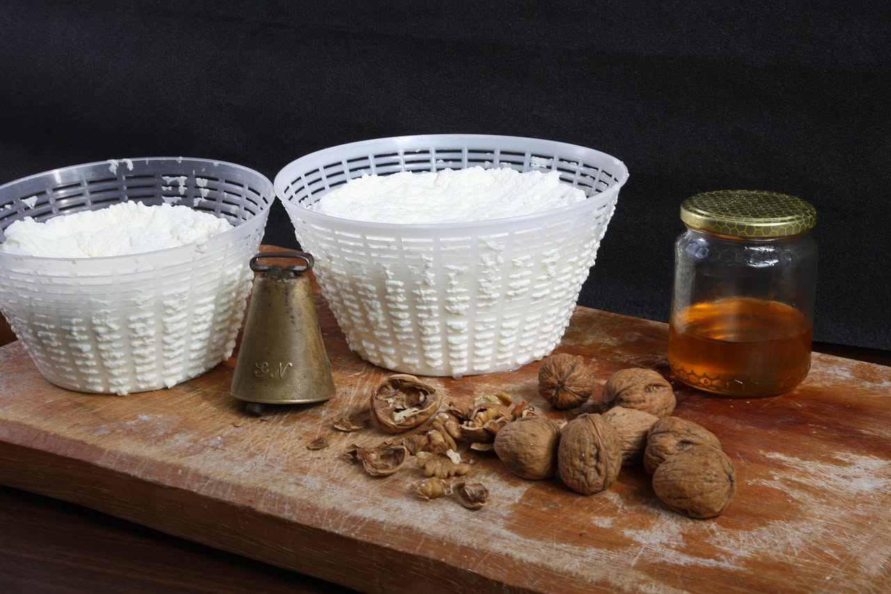 Ricotta bianca e cremosa in una ciotola di ceramica bianca, con un cucchiaio di legno, su sfondo di lino naturale