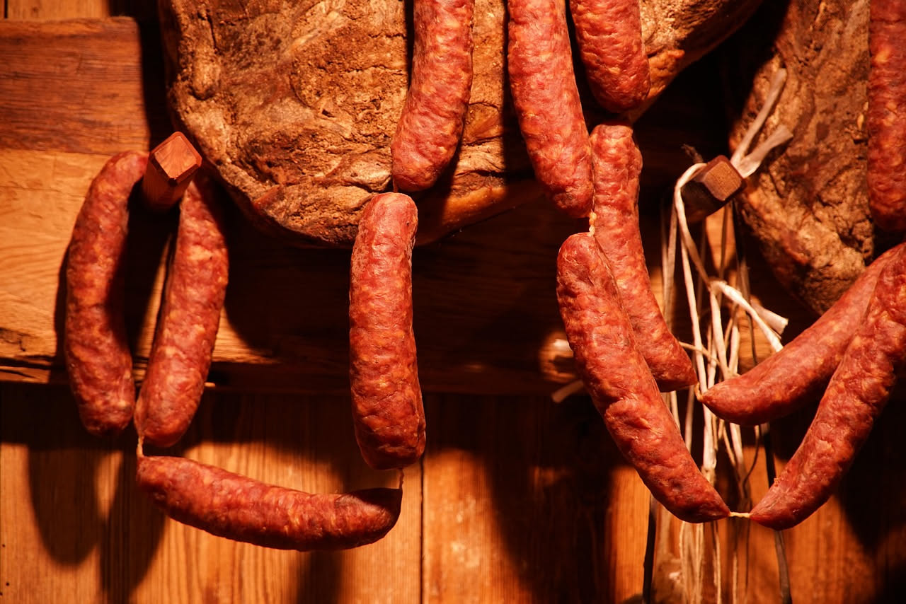 Salsicce fresche appena sfogliate, di colore bruno dorato, disposte su un tagliere di legno con rosmarino, aglio e peperoncino intorno