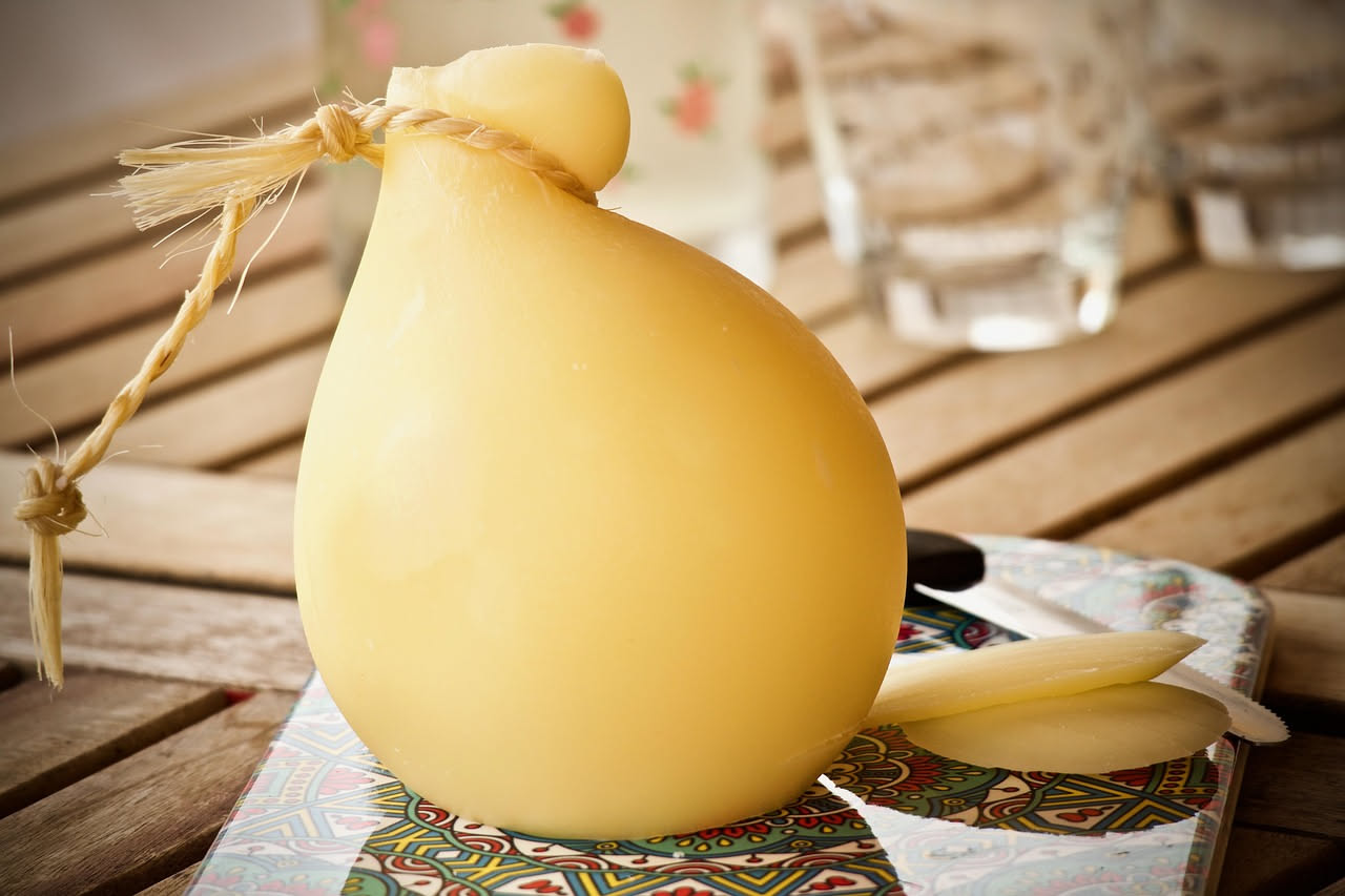 Scamorze fresche di forma tondeggiante con legaccio, disposte su un tagliere di legno con foglie di basilico fresco