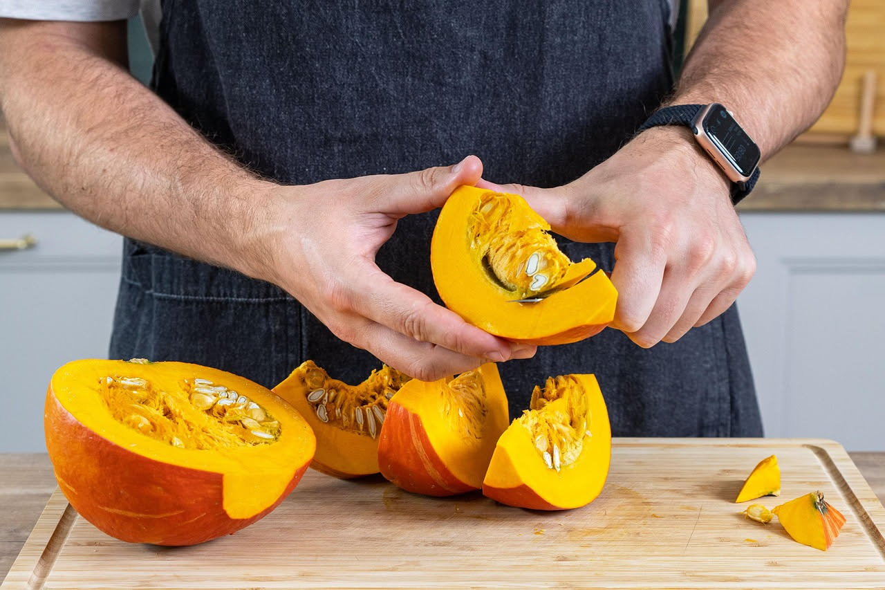 Zucche di diverse varietà, dal giallo al arancione, disposte su un tavolo di legno con foglie autunnali e un coltello da cucina