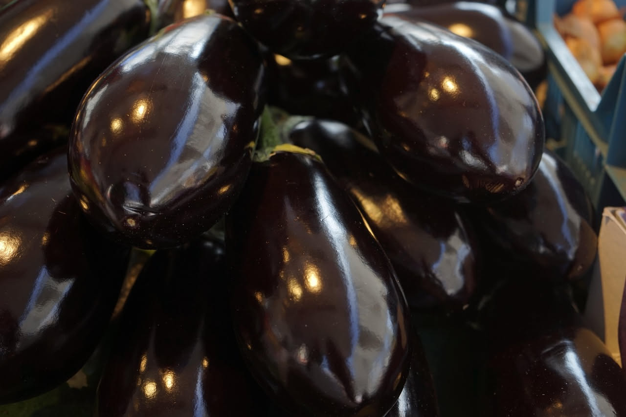 Melanzane violacee lucide e rotonde disposte su un tavolo di legno con foglie verdi e gambi, in luce naturale estiva