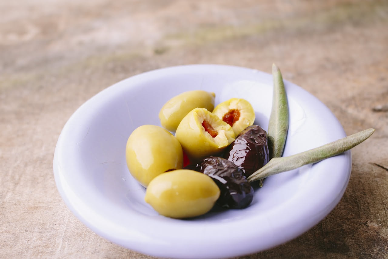 Olive verdi e nere appena colte su un ramo di olivo con foglie grigio-argento, in controluce, con sfondo di uliveto toscano