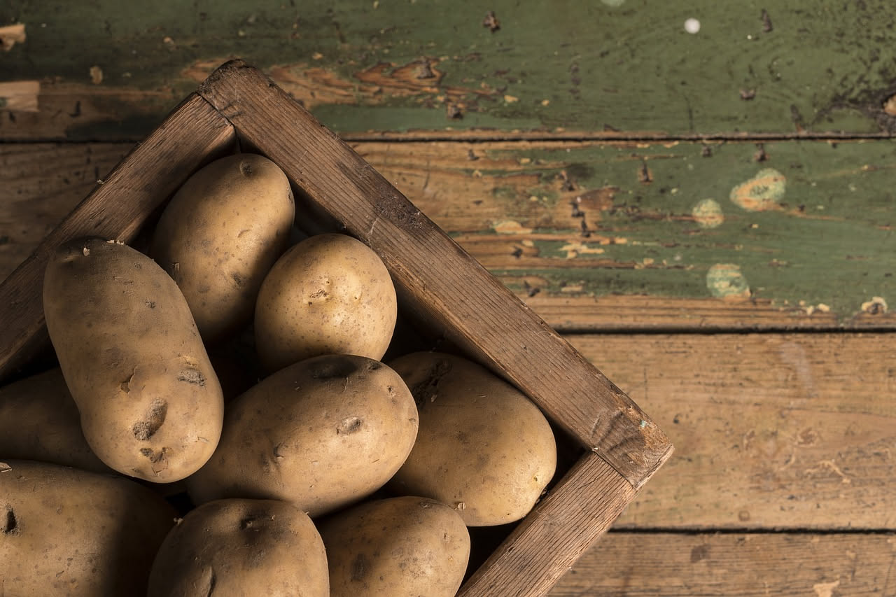 Patate di diverse varietà: rosse, bianche e gialle, disposte su un tavolo di legno rustico con foglie di prezzemolo fresco