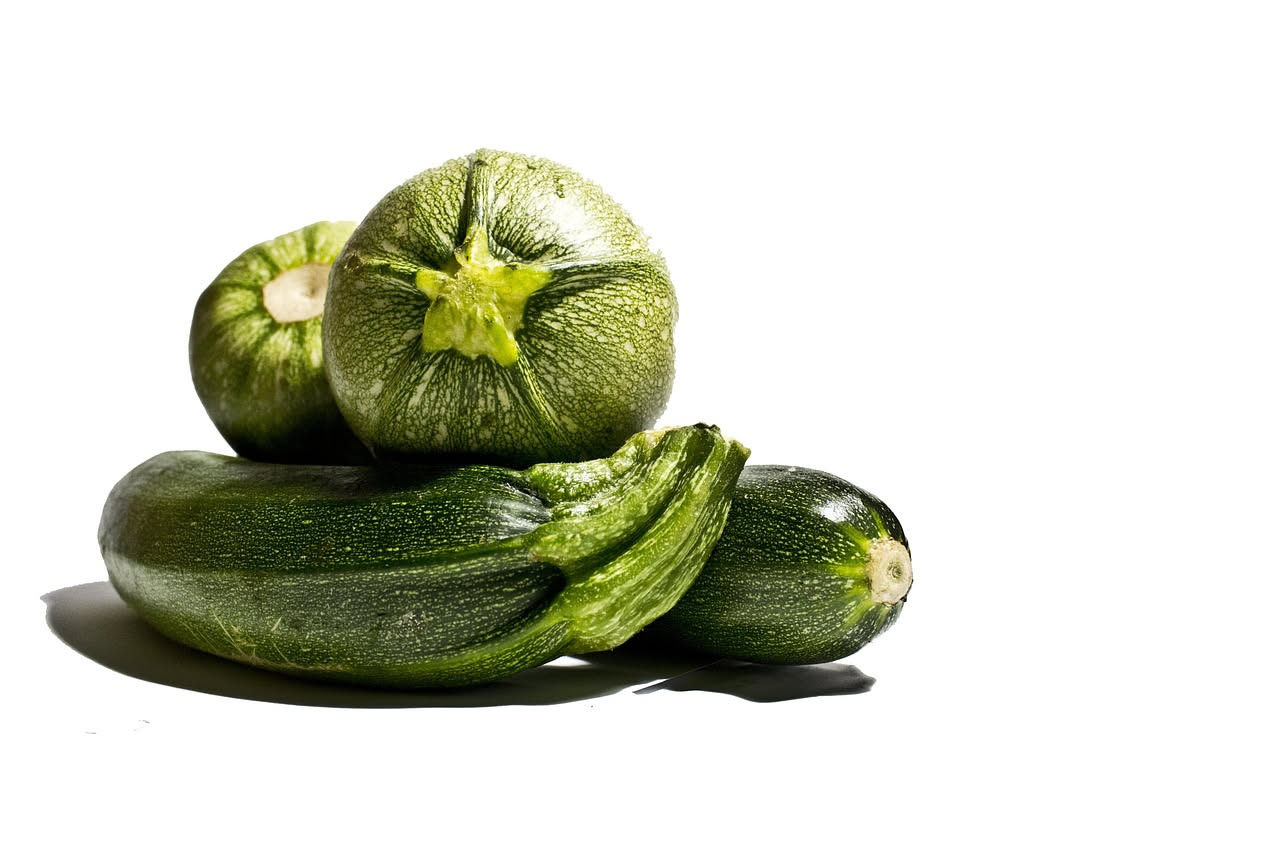 Zucchine verdi fresche appena colte, alcuni esemplari interi con fiore giallo ancora attaccato, disposti su un tavolo di legno con foglie di basilico fresco