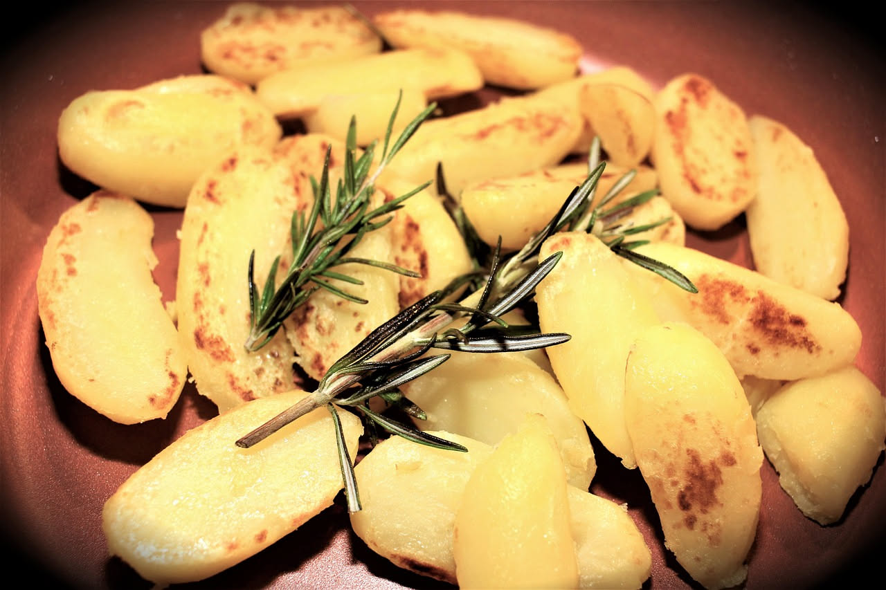 Patate dorate al forno in teglia accanto a una ciotola di purè cremoso con burro fuso e prezzemolo fresco, tavolo di legno scuro