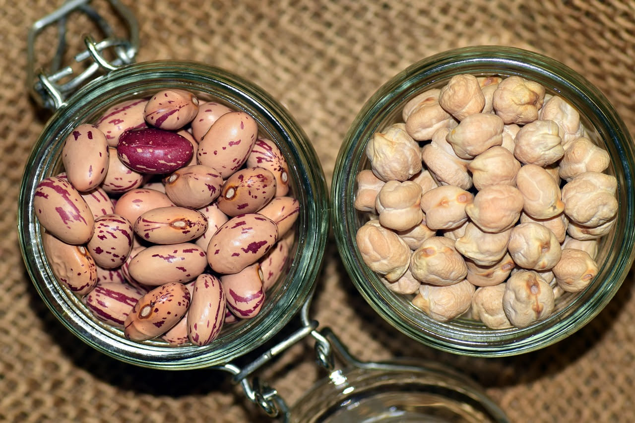 Ciotola di legumi secchi misti (fagioli, ceci, lenticchie) in ammollo in acqua limpida, accanto a un cucchiaio di legno e un orologio da cucina