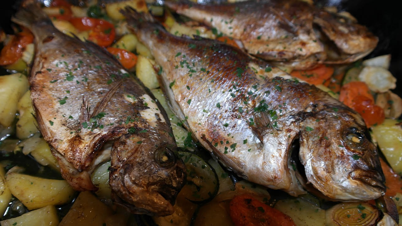 Filetto di branzino cucinato al cartoccio in carta pergamena con limone, erbe aromatiche e verdure grigliate su un piatto bianco