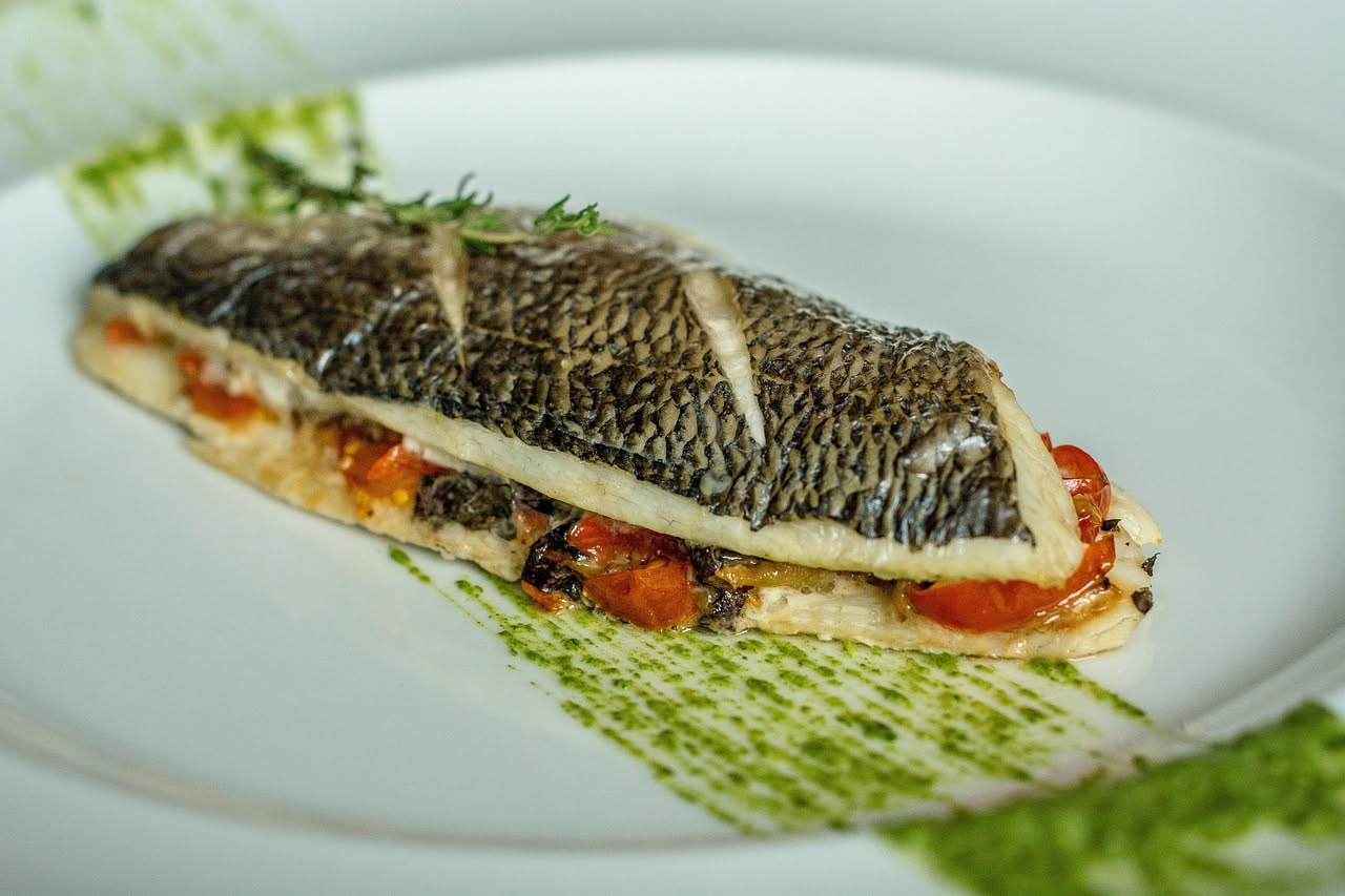 Filetto di pesce bianco con pelle dorata e croccante in padella antiaderente, con gocce d'olio lucido e limone affettato accanto