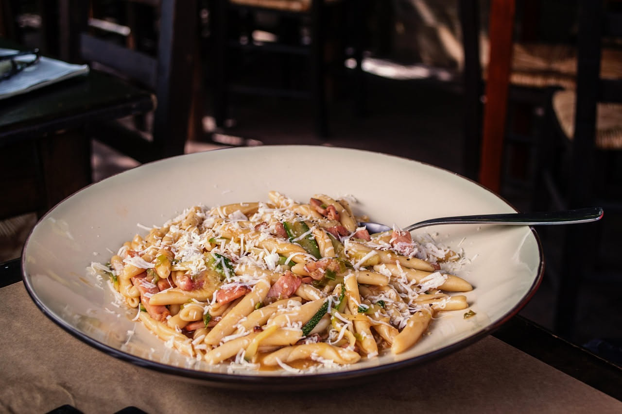 Piatto bianco con pasta al dente condita con zucchine verdi tagliate julienne e gamberi rosa pallido, guarnito con prezzemolo fresco verde, su sfondo neutro