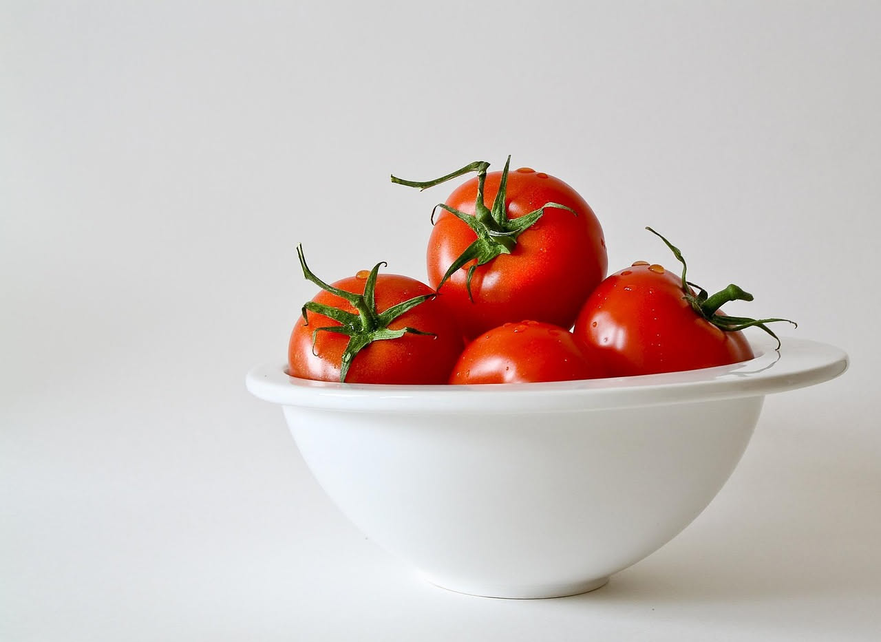 Pomodori rossi maturi su un piano di legno al sole in una cucina luminosa, accanto a una bottiglia d'olio d'oliva