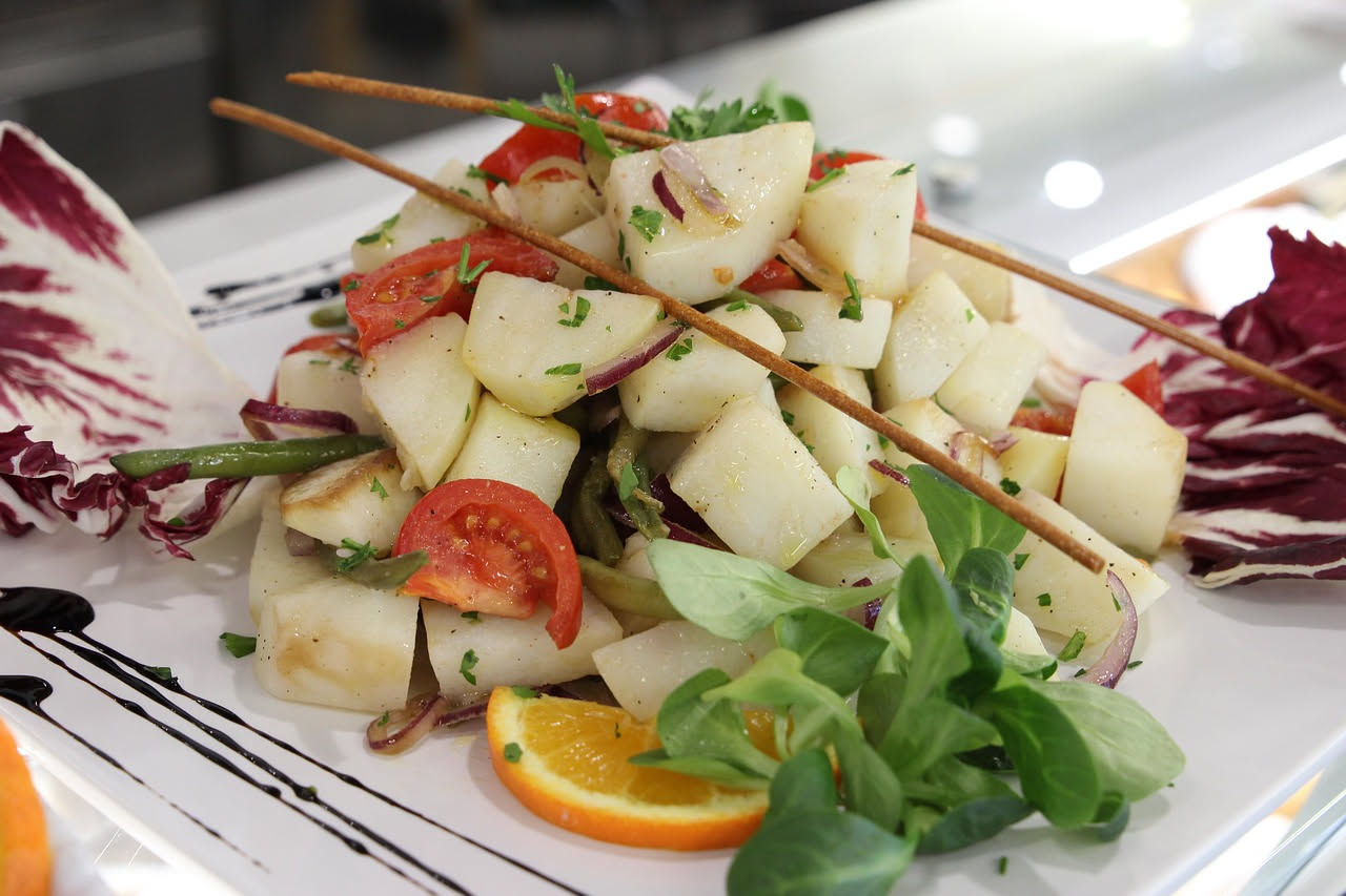 Insalata pantesca servita in un piatto bianco con pomodori rossi a dadini, pane tostato croccante, capers verdi e olive scure, condita con olio d'oliva dorato