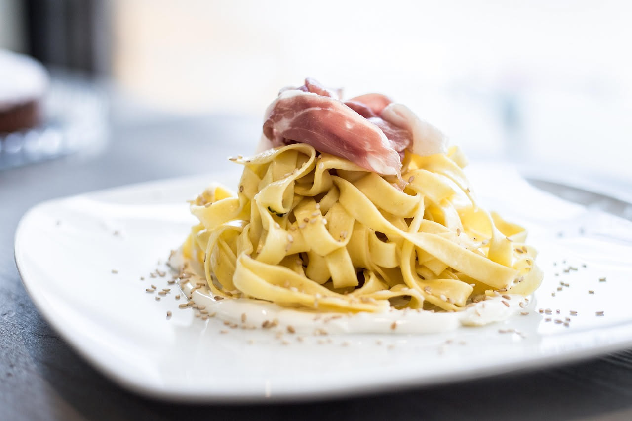 Piatto bianco con pasta lunga avvolta in ricotta cremosa bianca, cosparsă di pepe nero macinato, guarnito con una foglia di prezzemolo, servito su tavolo di legno chiaro