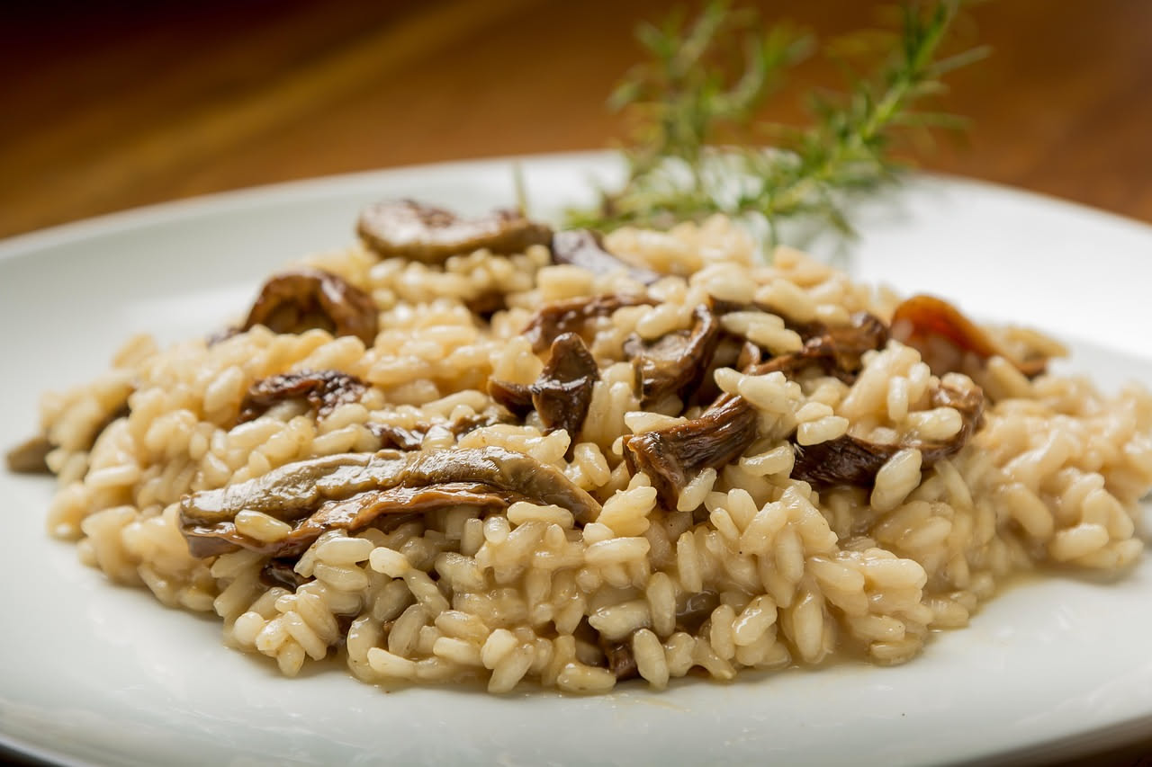 Risotto ai carciofi servito in piatto bianco fondo, colore bianco panna con sfumature verdi dai carciofi, grana grattugiata in superficie, cucchiaio di legno poggiato sul bordo