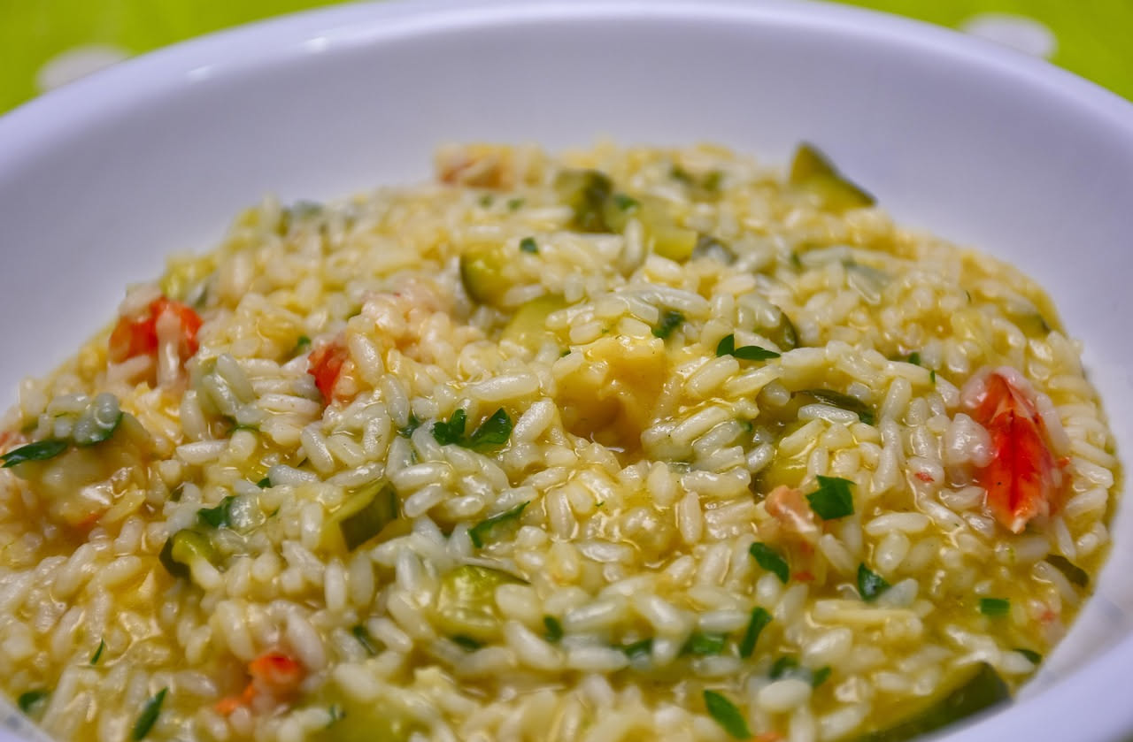 Risotto al limone in piatto bianco rotondo, cremoso di colore bianco avorio con puntini di scorza di limone giallo vivo, foglioline di menta fresca sul bordo, cucchiaio in acciaio inox appoggiato sul 