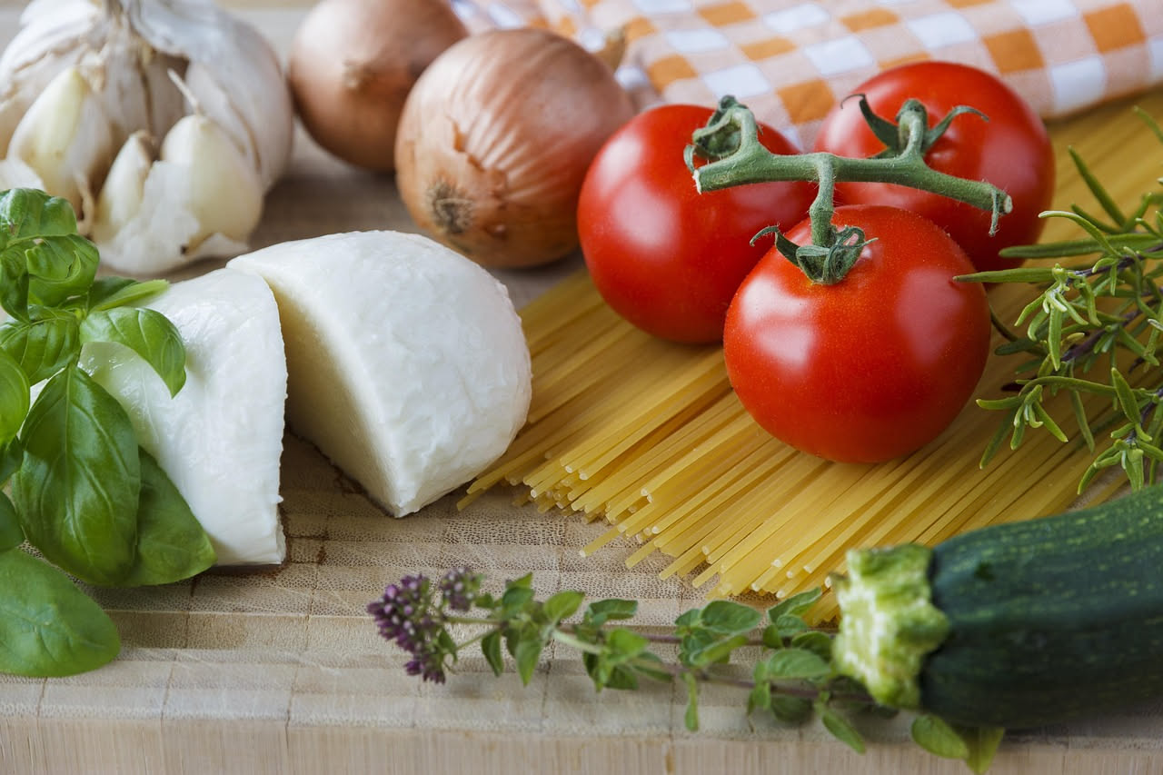 Piatto di spaghetti freddi con pomodori rossi e dadi di pomodoro crudo, basilico verde, gocce di olio dorato, servito su piatto bianco con bicchiere di acqua fredda sullo sfondo