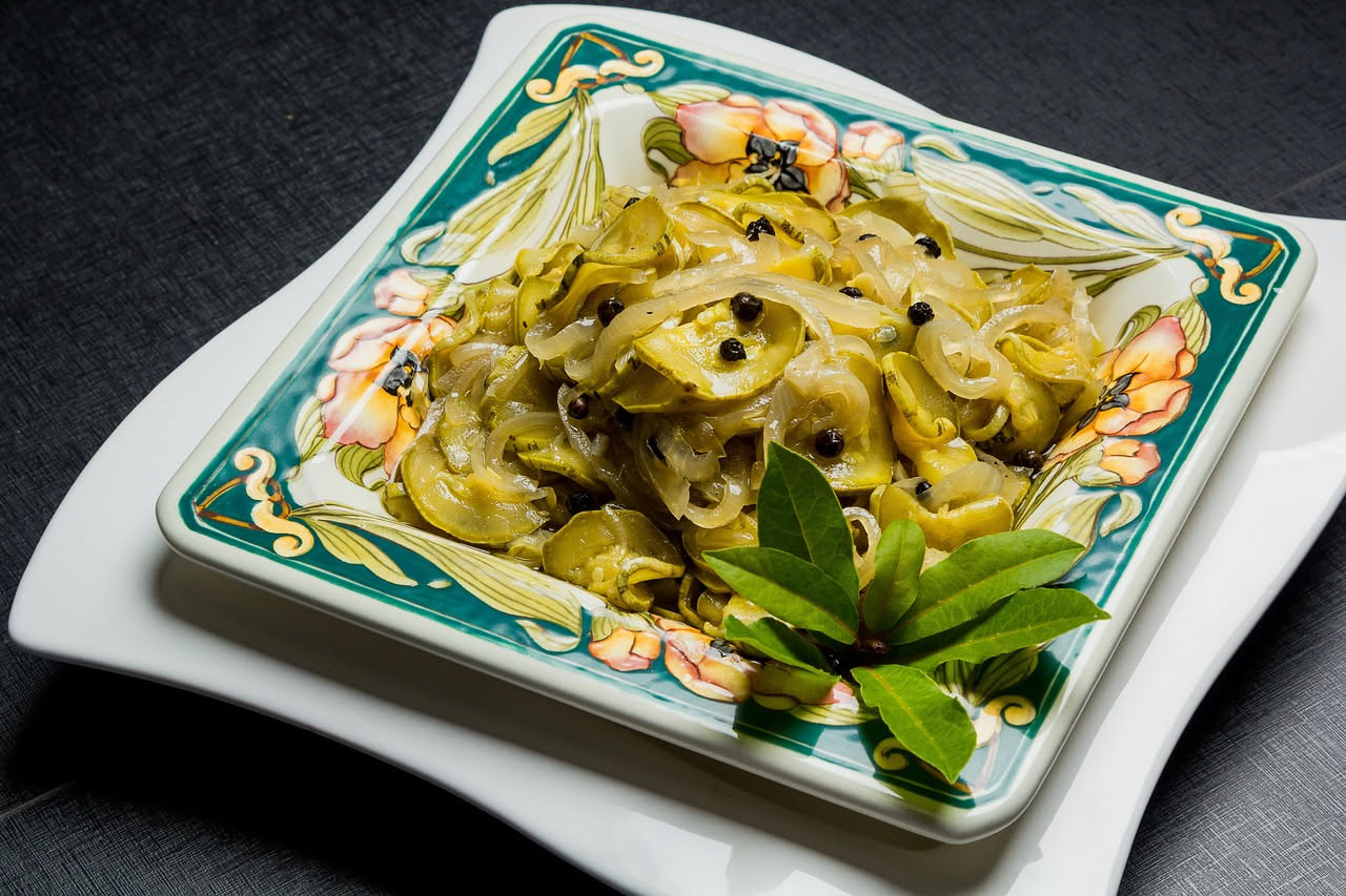 Piatto bianco con zucchine verdi affettate sottilissime disposte a ventaglio, condite con gocce di olio dorato, petali di menta fresca e scaglie di parmigiano, limone fresco a lato