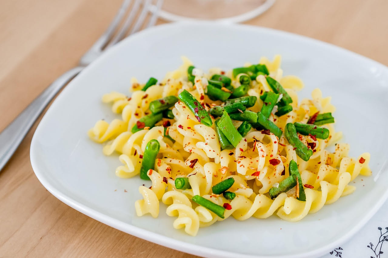 Insalata di patate bianche e gialle a dadini con fagiolini verdi tesi, pomodori rossi a pezzetti, prezzemolo fresco e olio d'oliva, servita in una ciotola bianca su tavolo di legno chiaro con luce nat