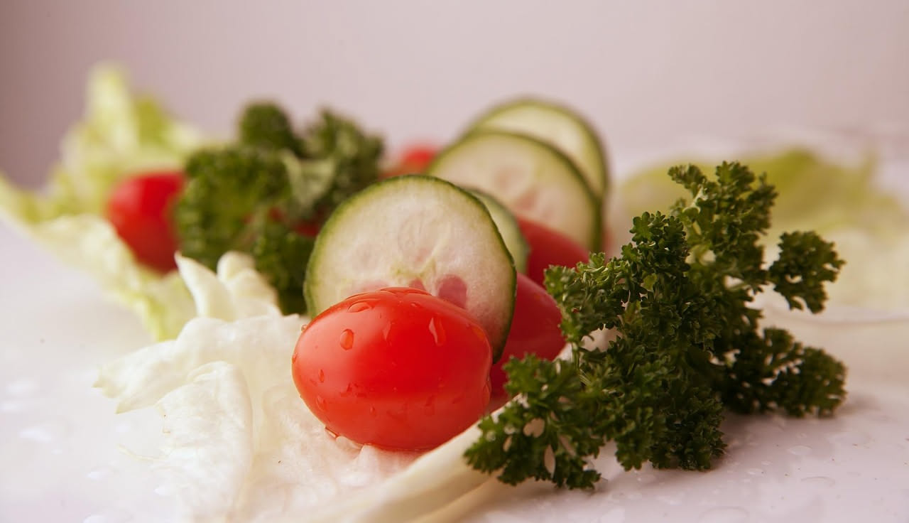 Insalata di pomodori rossi tagliati a spicchi e cetrioli verdi affettati disposti in una ciotola bianca, con basilico fresco e gocce d'olio d'oliva, su un tavolo di legno chiaro con luce naturale