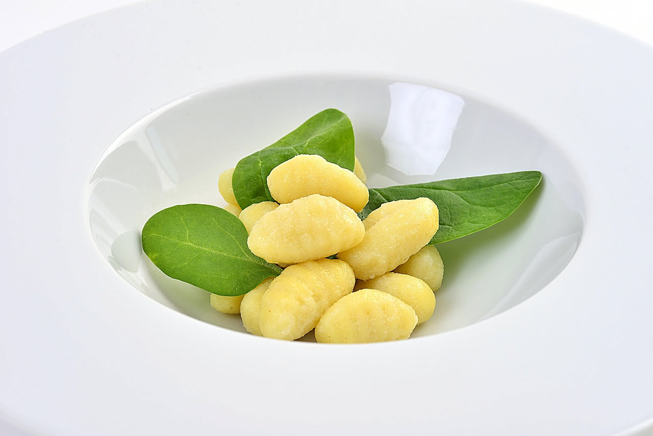 Piatto di gnocchi di patata conditi con burro fuso, foglie di salvia fresca e parmigiano grattugiato, su fondo neutro