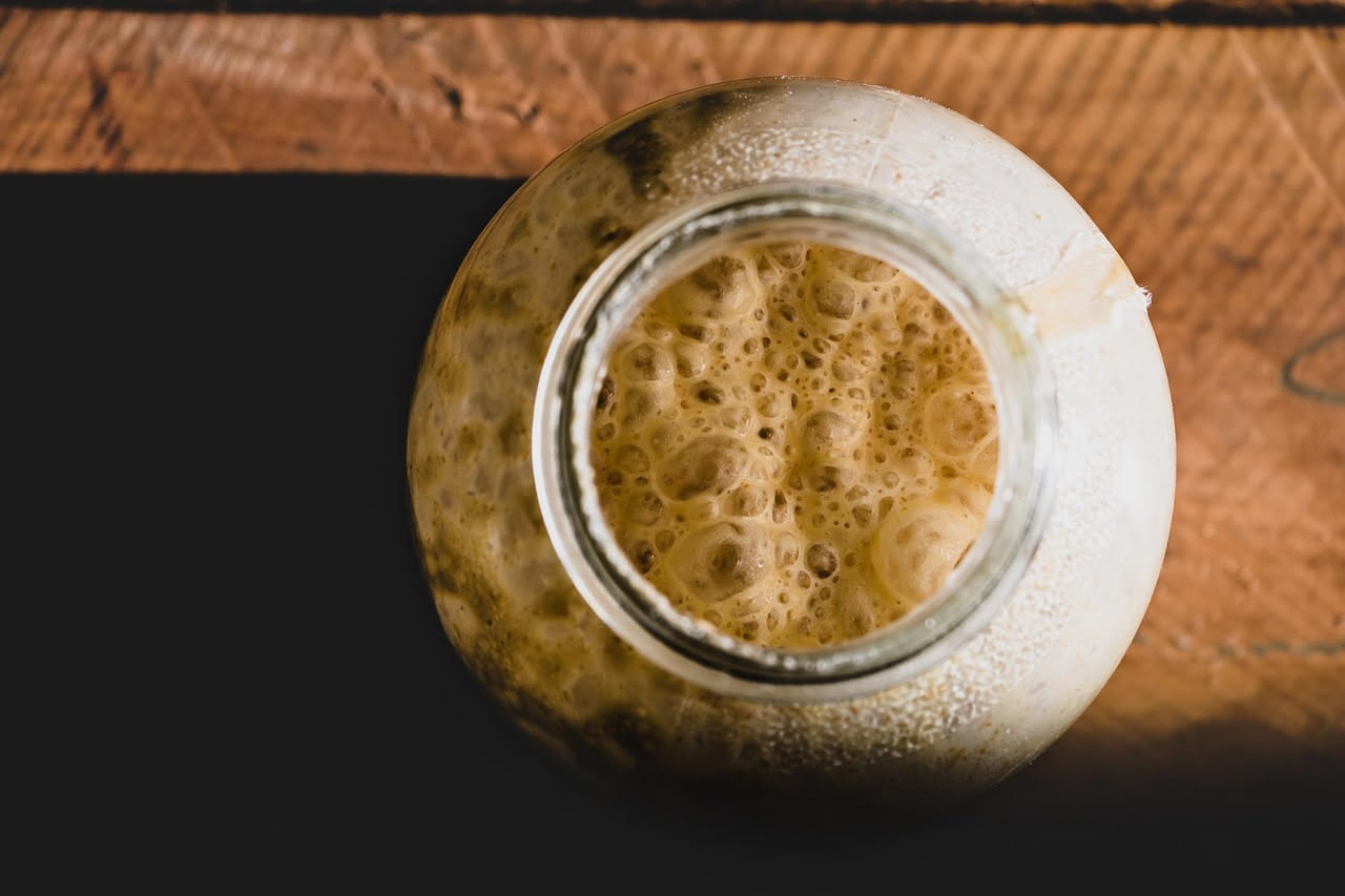 Tre ciotole bianche su un banco di marmo contengono rispettivamente un lievito madre cremoso e grigio, cubetti di lievito di birra fresco brunastri e polvere di lievito istantaneo color sabbia.