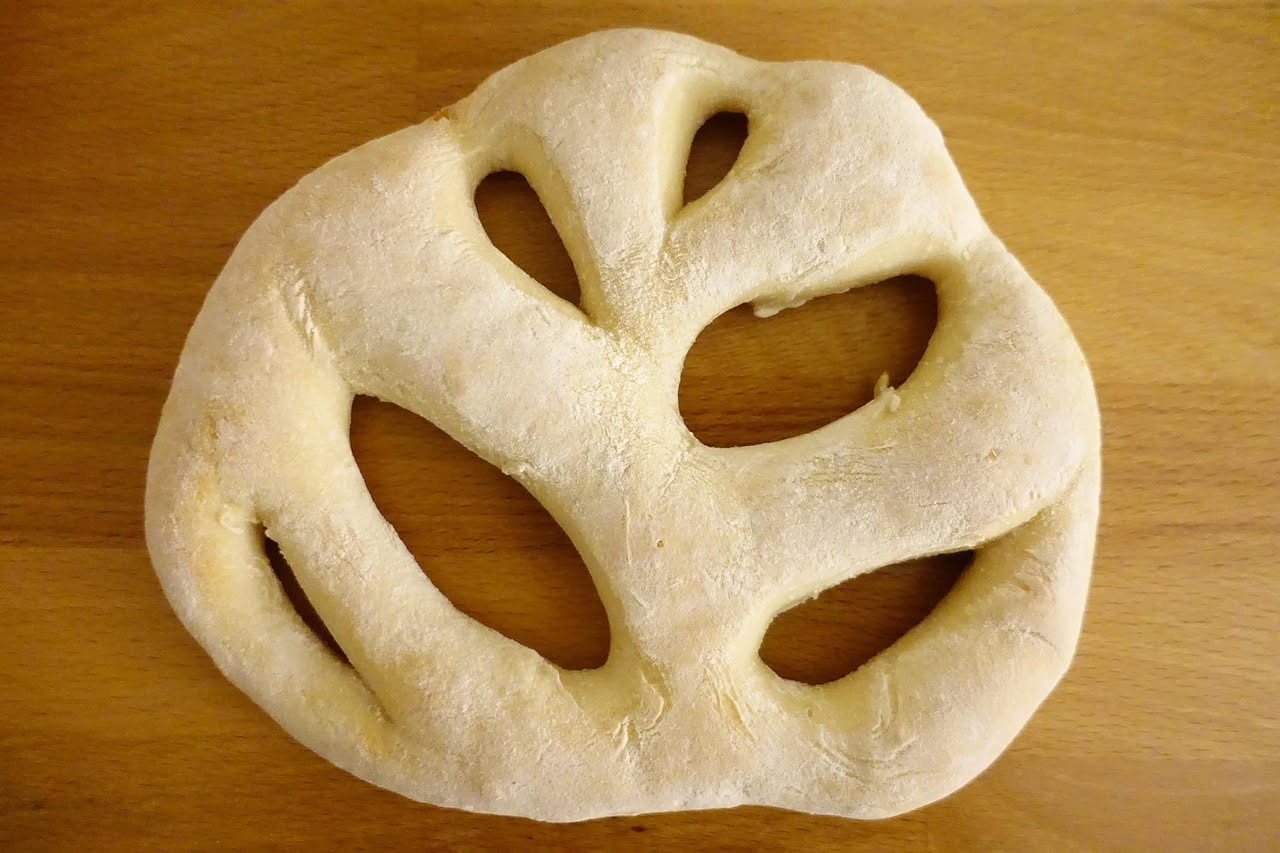 Mani che impastano farina e acqua su un tavolo di marmo bianco, con una ciotola di terracotta sullo sfondo e ingredienti ordinati accanto
