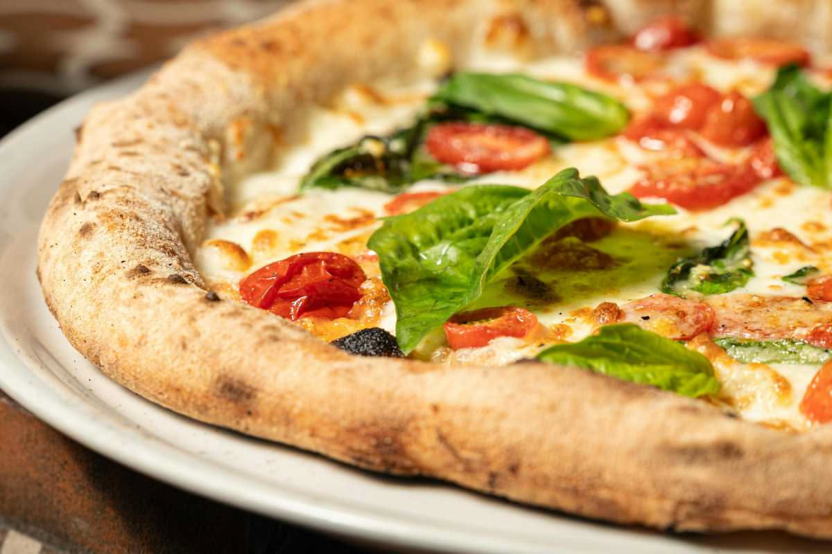 Pizza appena sfornata con cornicione dorato, pomodoro fresco e basilico verde su una pala di legno in cucina domestica