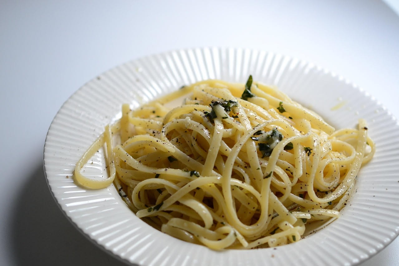Linguine dorate in un piatto bianco, ricoperte di menta verde fresca strappata e buccia di limone grattugiata, condite con olio brillante, servite con un quarto di limone giallo limone di lato