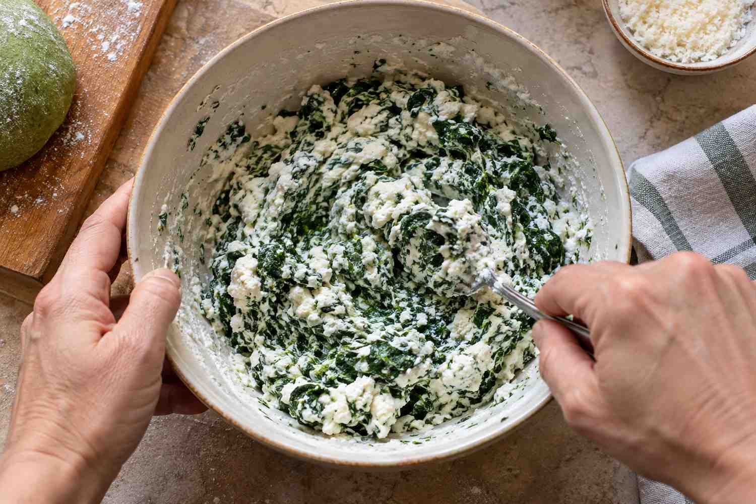 Una ciotola bianca con ricotta e spinaci tritati mescolati con una forchetta