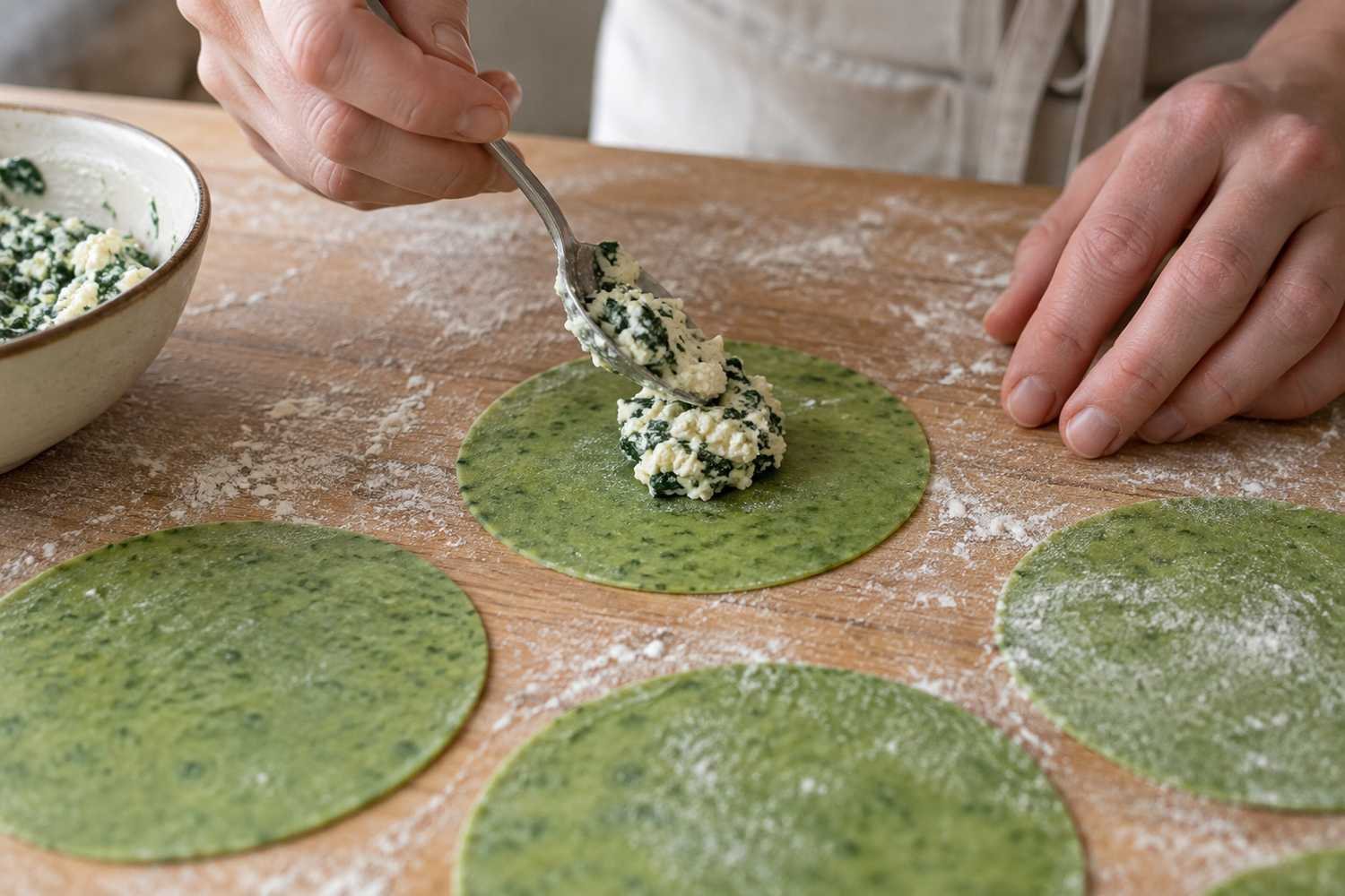 Un cucchiaino posa il ripieno di ricotta e spinaci al centro di dischi di sfoglia verde