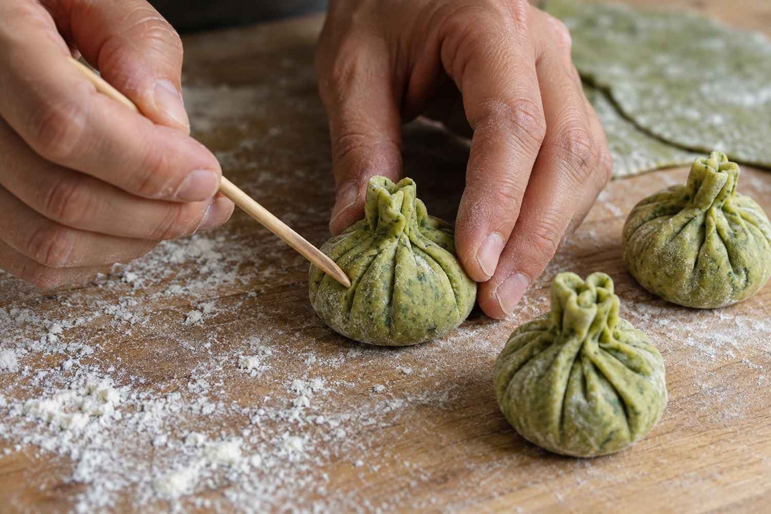 Le mani modellano con uno stecchino le scanalature di un fagottino verde accanto ad altri già pronti