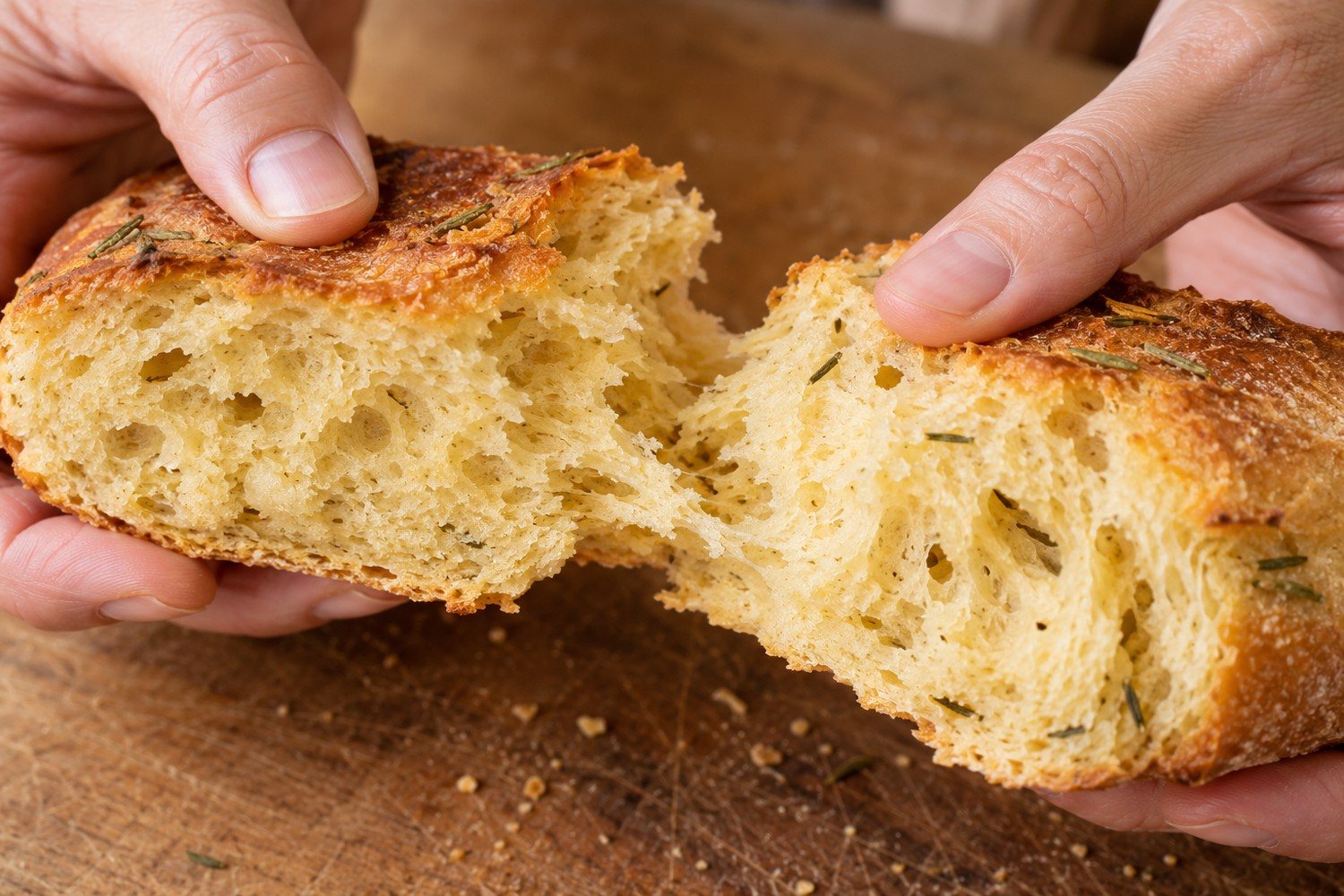 Due mani aprono un pezzo di pane con crosta dorata e mollica gialla piena di piccoli alveoli